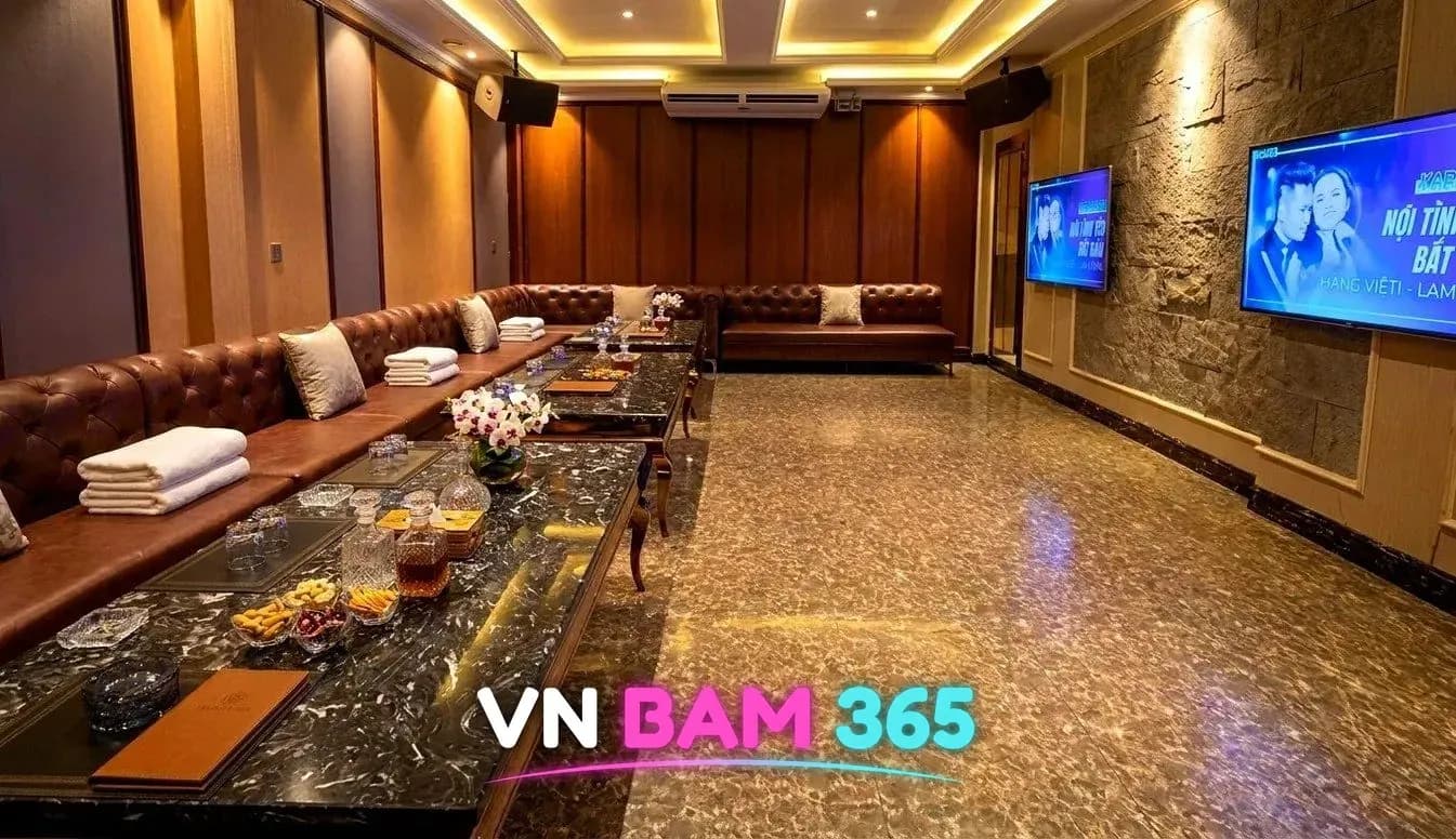 다낭 아우디 가라오케 대형 룸, 갈색 가죽 소파가 길게 놓이고 수건과 꽃이 놓인 대리석 테이블, 벽걸이 화면 두 대