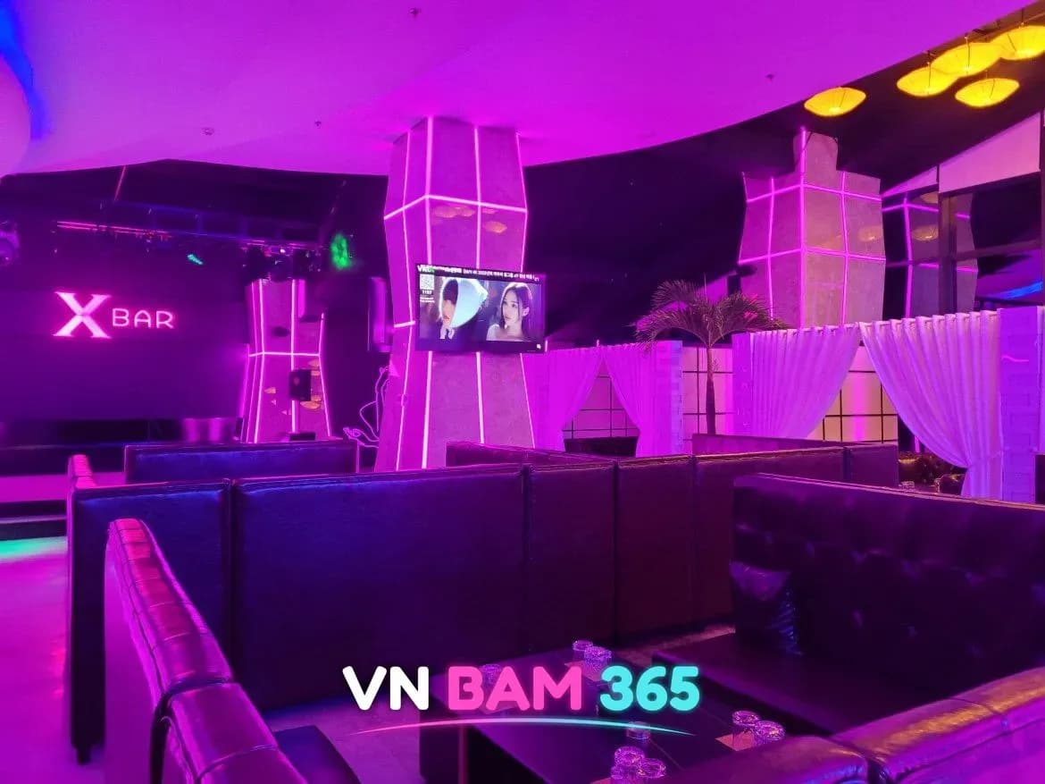 다낭 엑스바 라운지, 분홍 조명 아래 X BAR 네온 로고와 검은 가죽 소파석, 흰 커튼으로 나뉜 좌석