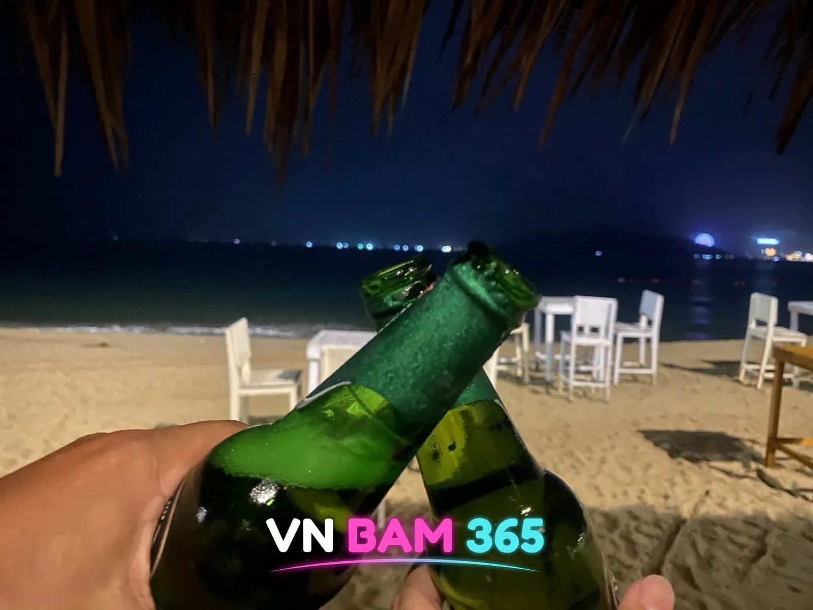 나트랑 해피 비치 야간 초가 차양 아래 병맥주 건배, 백사장 흰 테이블석과 바다 야경