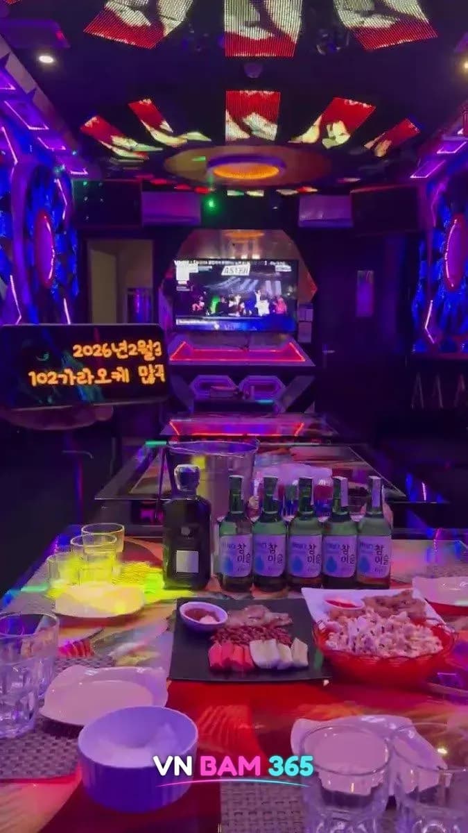 호치민 102 가라오케 룸 안 테이블에 차려진 소주병과 안주 접시, 정면 화면