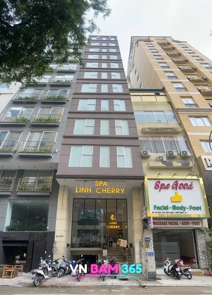 호치민 1군 타이반룽 거리 린체리 스파 외관, 고층 건물 1층 입구 위 SPA LINH CHERRY 금색 간판과 앞에 세워진 오토바이들