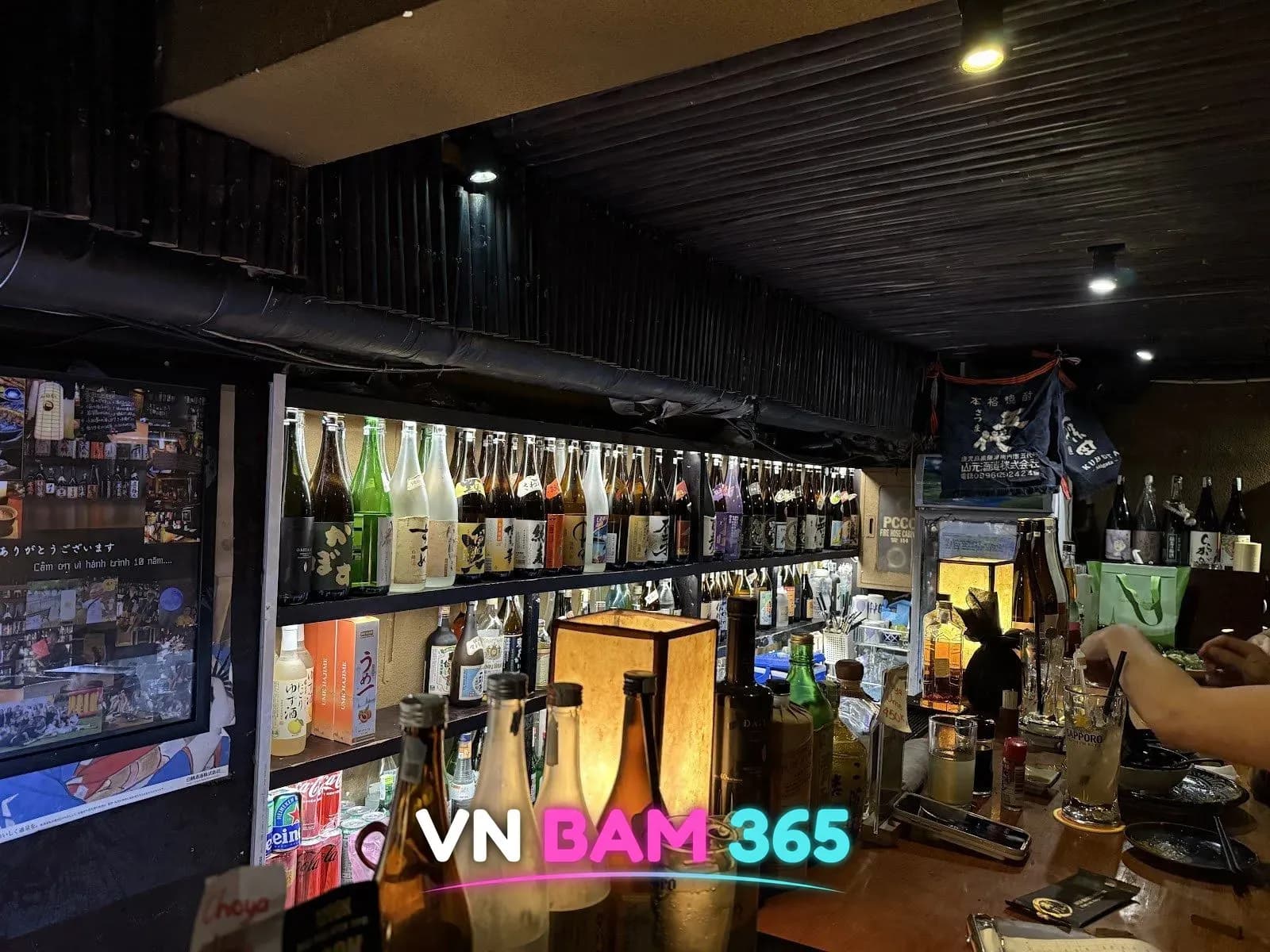 호치민 1군 망게츠 소주 바 카운터 뒤 일본 소주·사케 병이 빼곡한 조명 선반