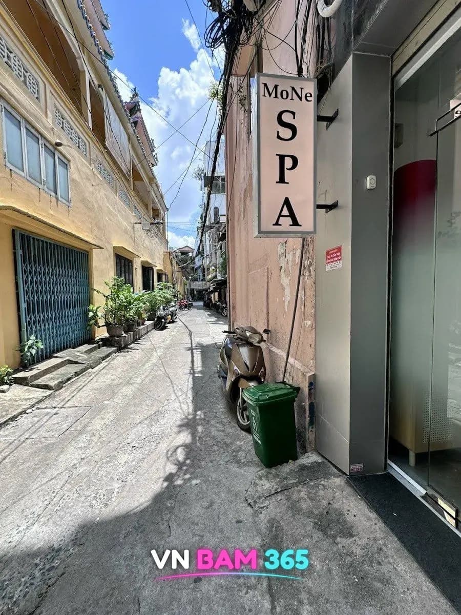 호치민 1군 모네 스파 골목 입구, MoNe SPA 세로 간판과 유리문, 맑은 하늘 아래 좁은 골목