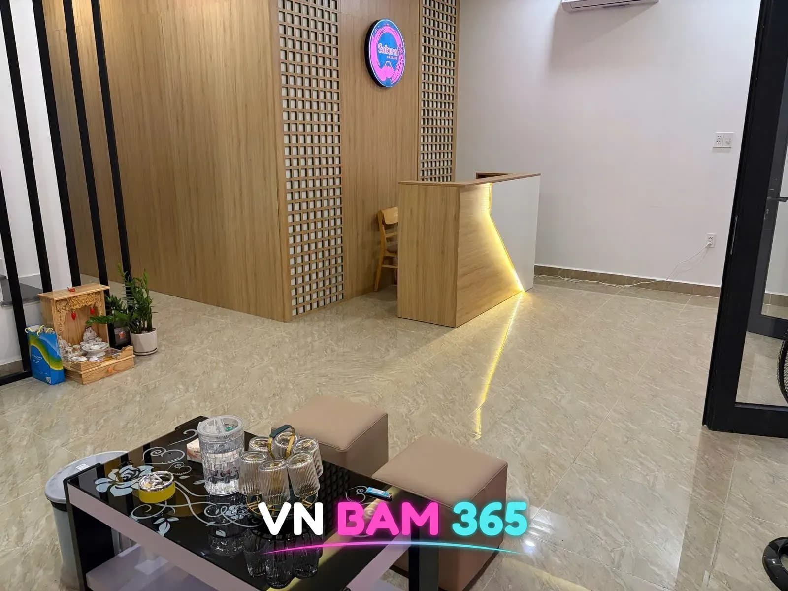 푸꾸옥 사쿠라 마사지 리셉션과 대기 공간, Sakura 로고 원목 벽과 데스크, 유리컵이 놓인 테이블