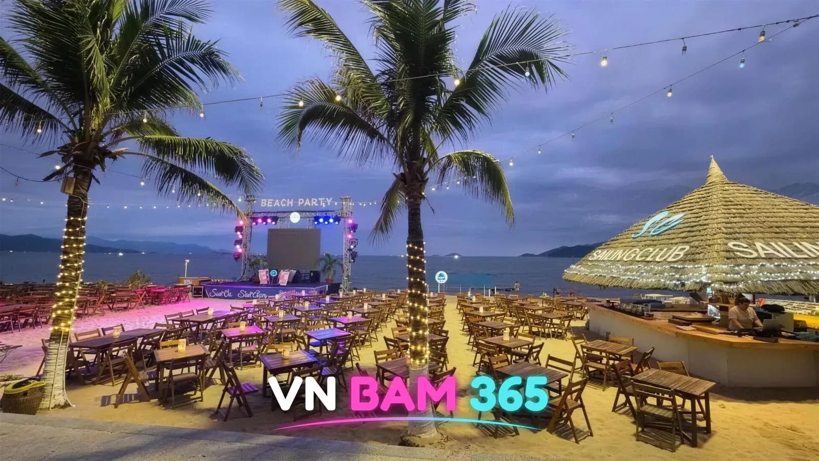 나트랑 세일링 클럽 해질녘 백사장 테이블석과 BEACH PARTY 무대, 초가지붕 바와 야자수 전구 조명