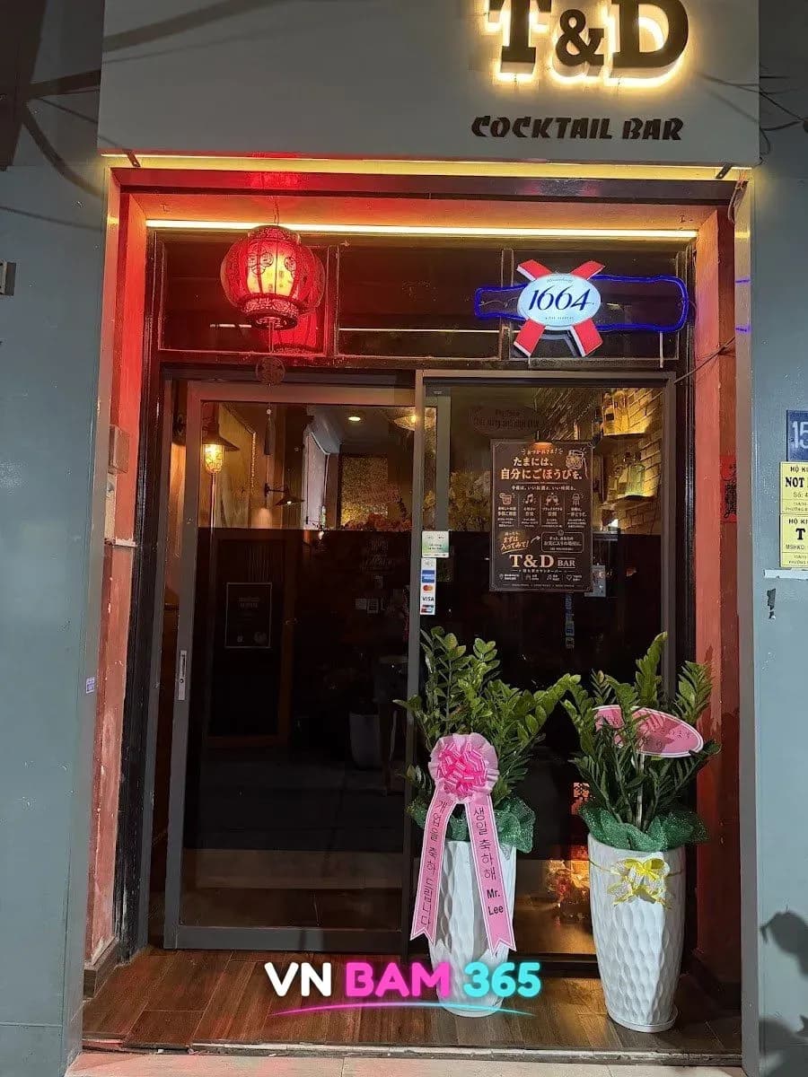 호치민 1군 레탄톤 골목 T&D 칵테일 바 야간 입구, 조명 간판과 붉은 등, 축하 화분