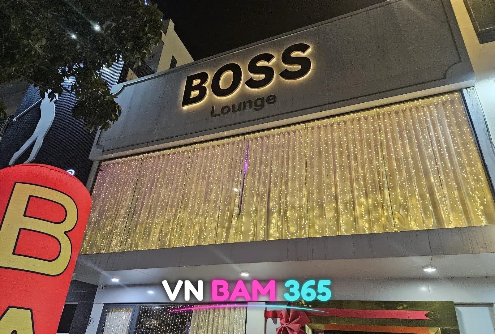 다낭 보스바 야간 외관, BOSS Lounge 입체 간판과 노란 전구 커튼으로 덮인 건물 전면