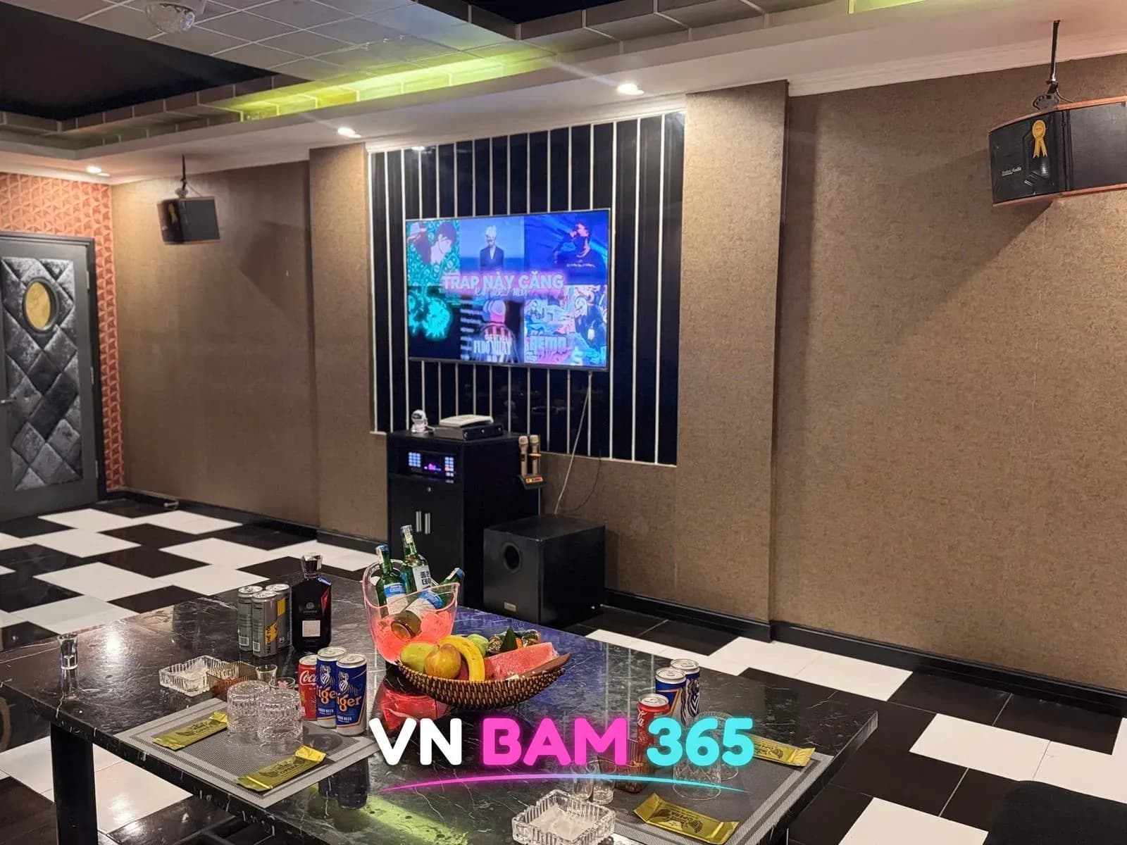 다낭 원오페라 가라오케 룸, 체크무늬 바닥과 노래방 화면, 과일 바구니와 캔맥주가 놓인 대리석 테이블