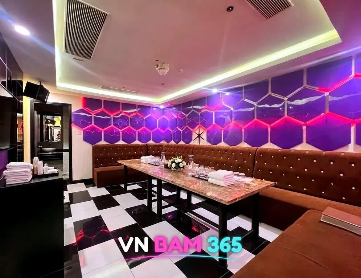 다낭 원오페라 가라오케 룸, 보라색 육각 패널 벽과 체크무늬 바닥, 긴 테이블과 갈색 소파