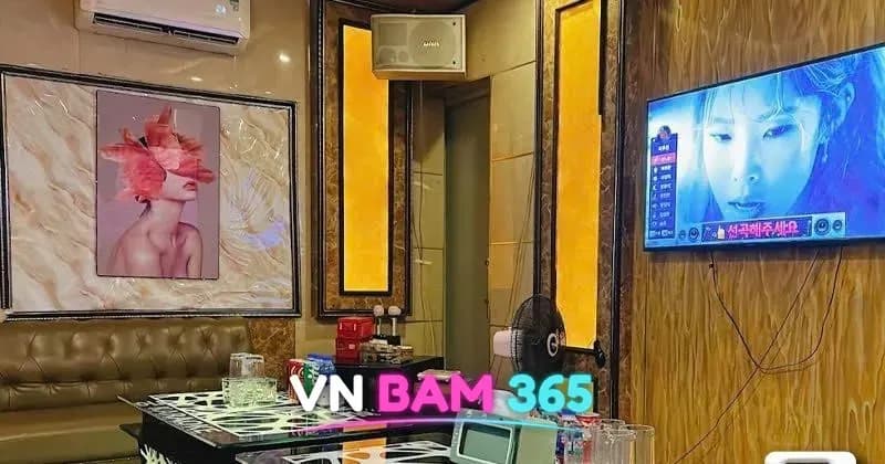 하노이 궁 가라오케 룸, 가죽 소파 옆 테이블에 음료와 리모컨, 벽걸이 노래방 화면
