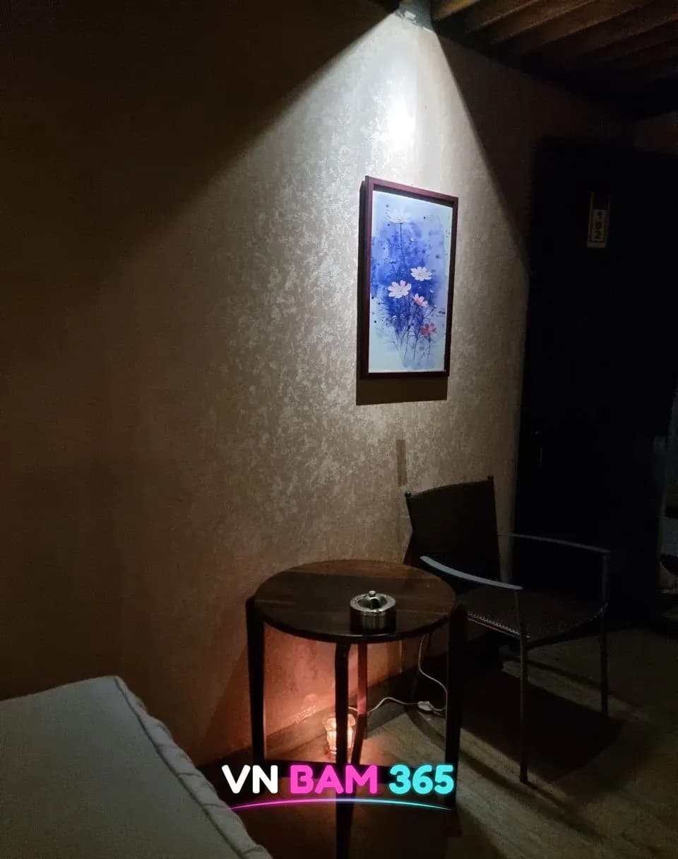 나트랑 화다4 마사지 객실 휴식 공간, 파란 꽃 그림 액자 아래 원목 원형 탁자와 라탄 의자
