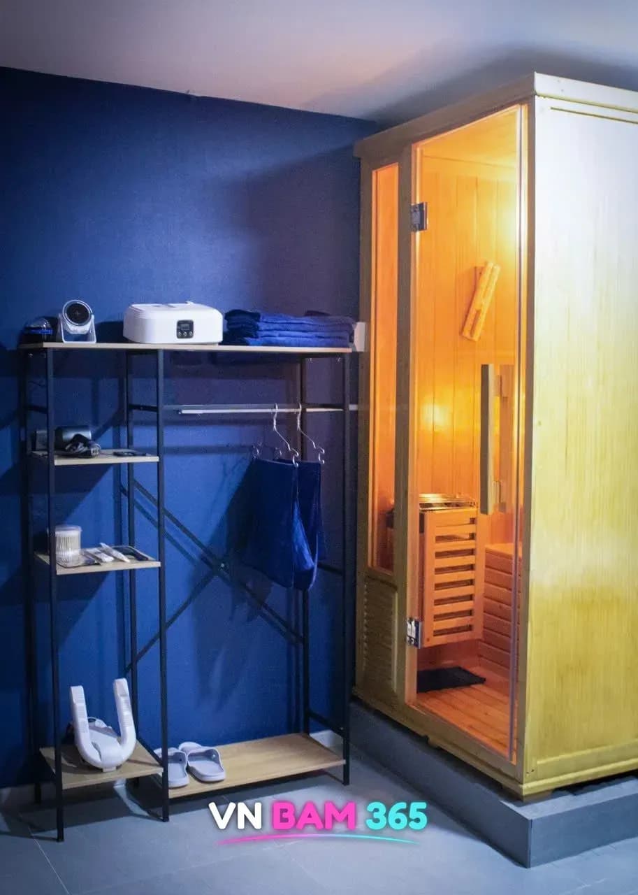 호치민 킹스톤 마사지 객실의 원목 1인 사우나와 수건·헤어드라이어·슬리퍼가 놓인 비품 선반