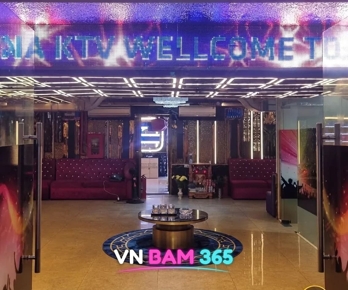 나트랑 갈리나 가라오케 입구, KTV WELLCOME 전광판 아래 유리문 너머 붉은 소파와 원형 테이블이 놓인 로비