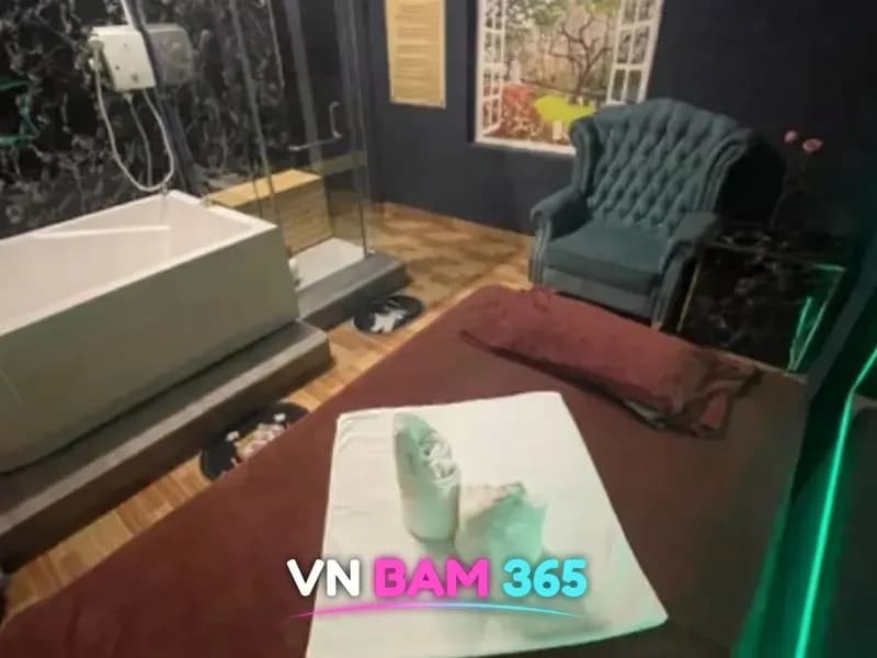 호치민 스타킹 마사지 개인실, 마사지 베드 위 수건과 사각 욕조, 유리 샤워 부스와 녹색 소파